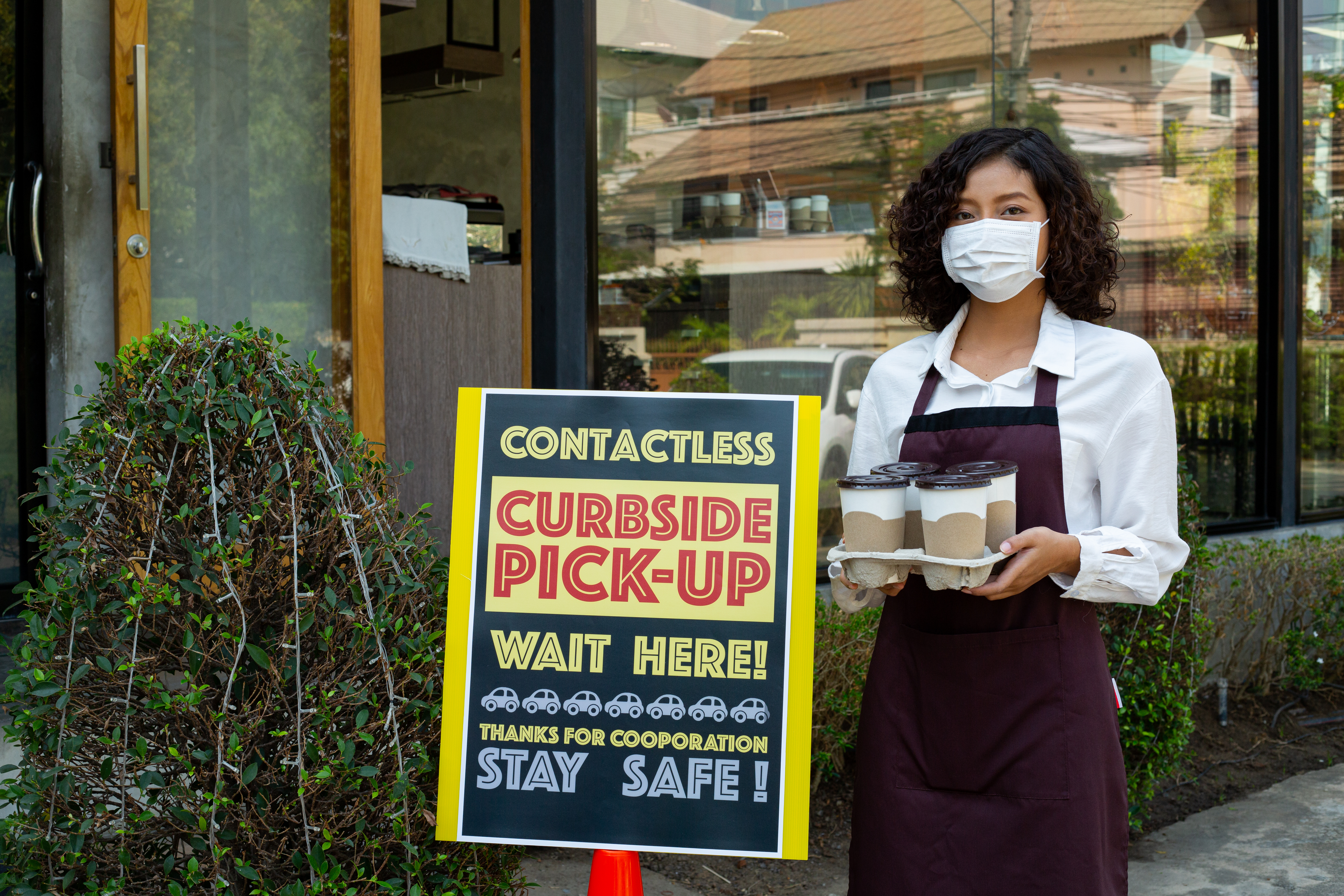 Women with Coffees standing beside Curbside Pickup Sign